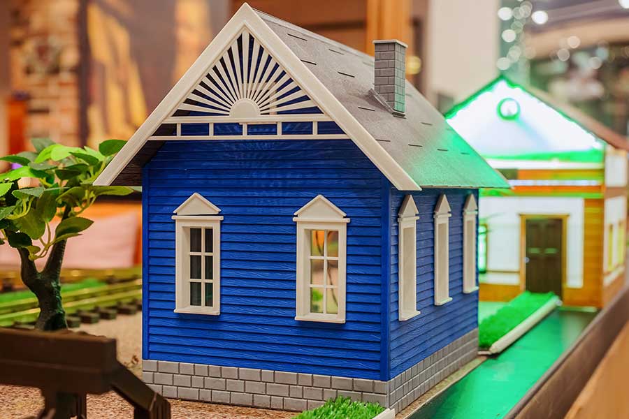 A detailed blue model house with white trim and a peaked roof.