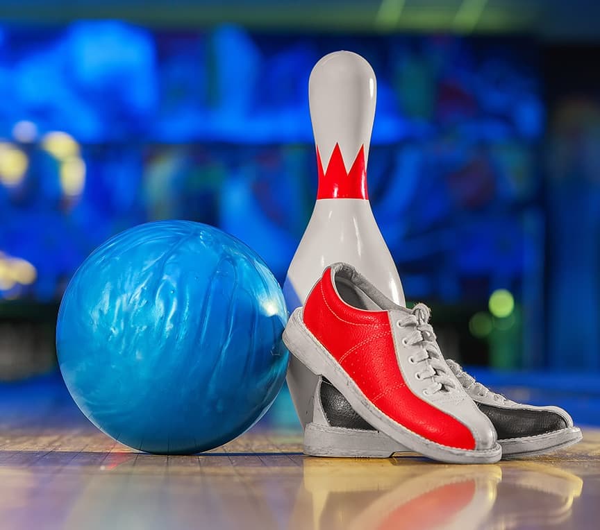 A blue bowling ball, red and gray bowling shoes, and a standing bowling pin are arranged on a wooden lane.
