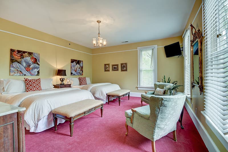 A cozy hotel room featuring two beds, a seating area, and decorative artwork on yellow walls.