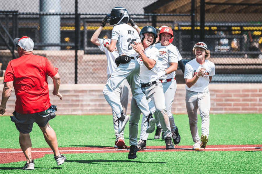 A group of young baseball players celebrate joyfully after a game, with one player being lifted off the ground in excitement.