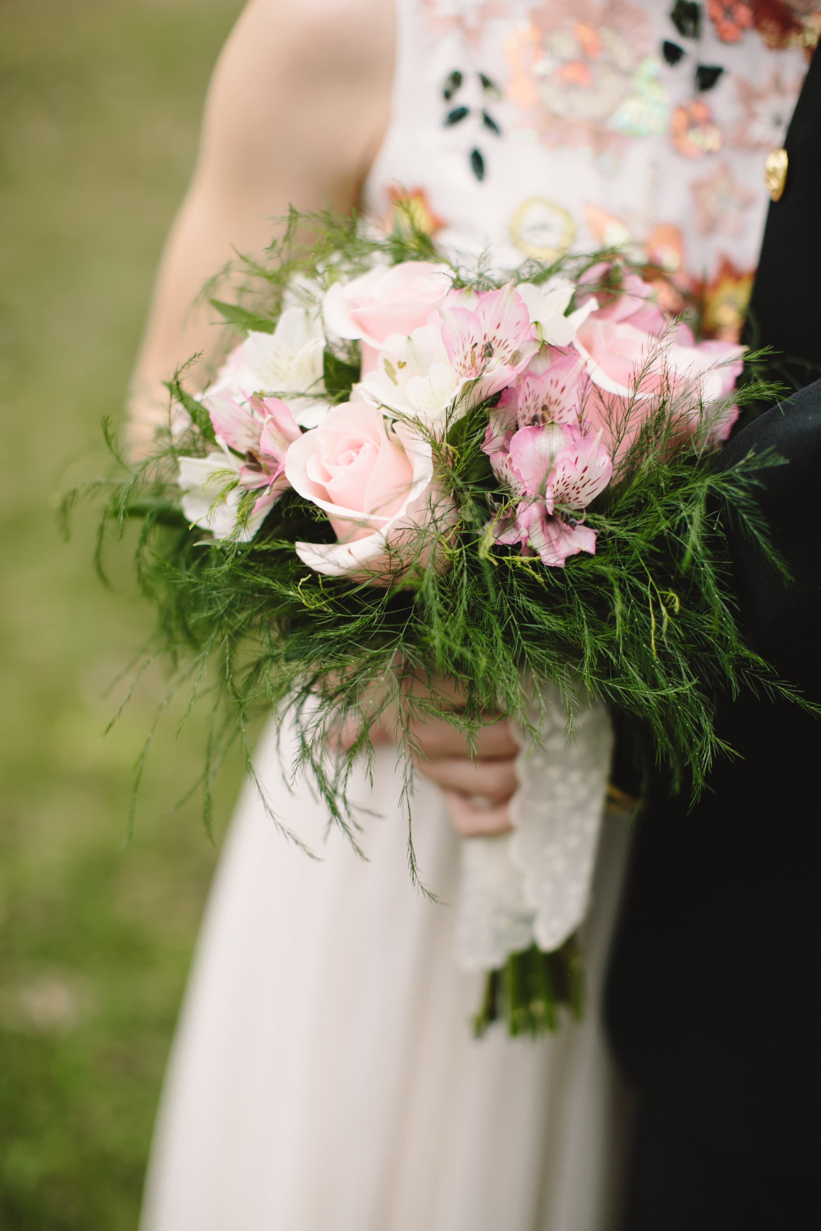 A close-up of a person holding a lush bouquet of pink roses and white flowers with green foliage.