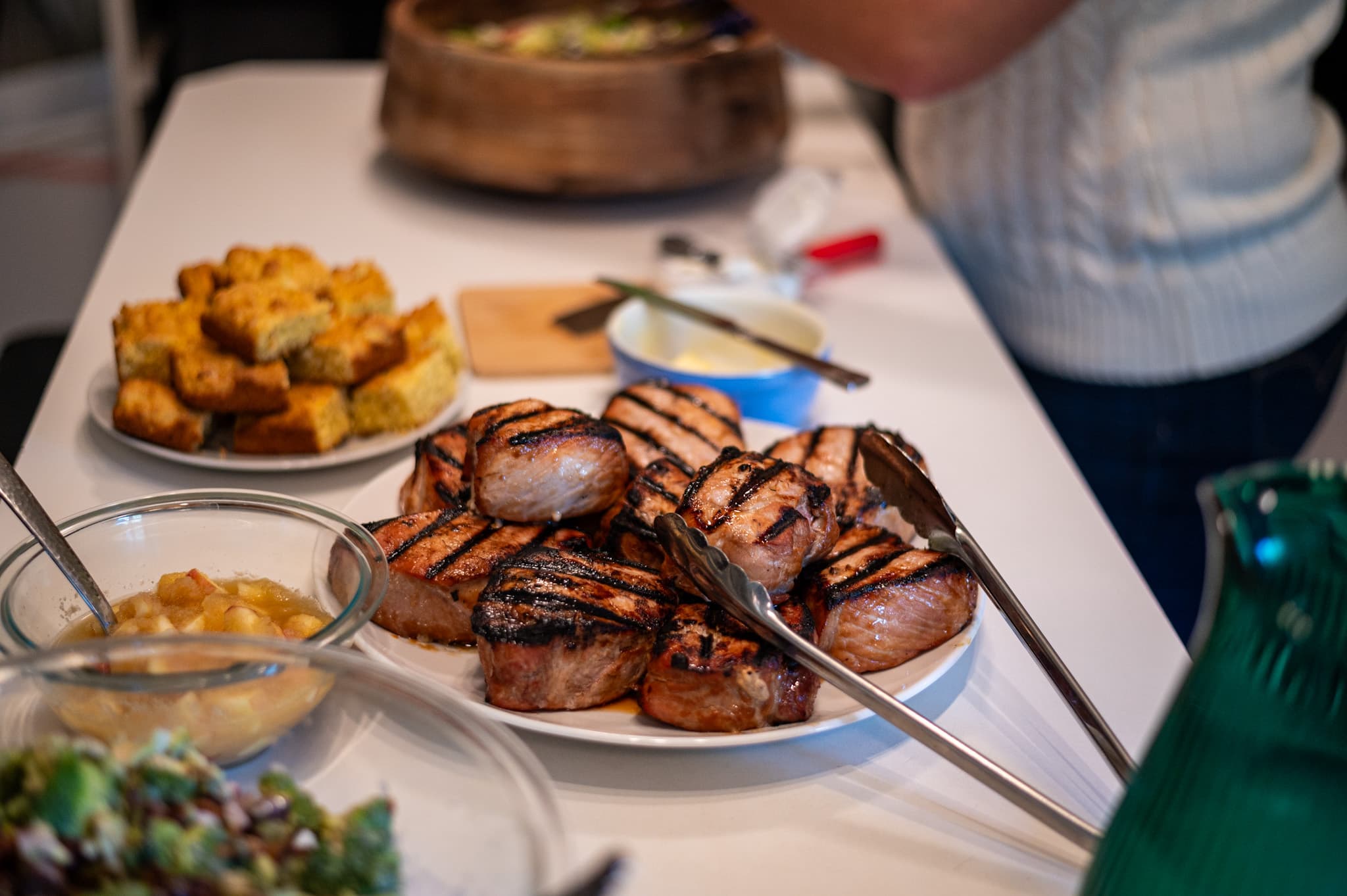 A table with grilled pork chops, cornbread, salad, and various condiments.