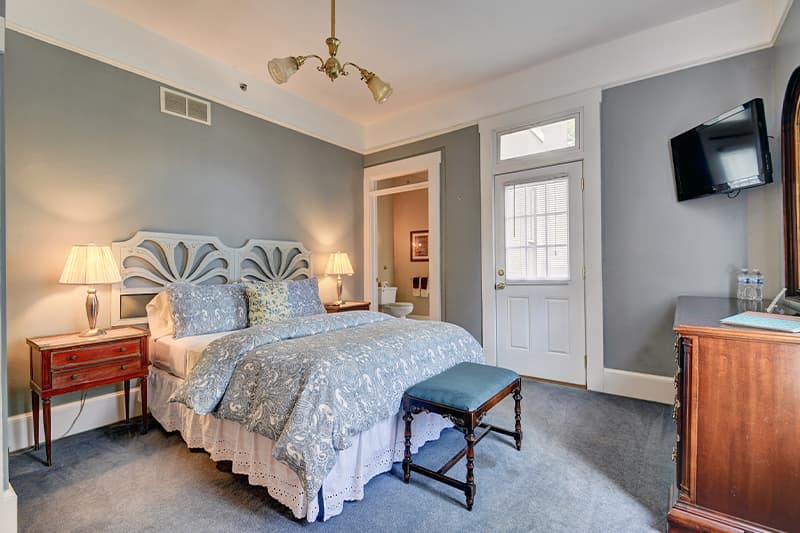 Cozy bedroom featuring a queen bed, bedside tables with lamps, and a TV mounted on the wall.