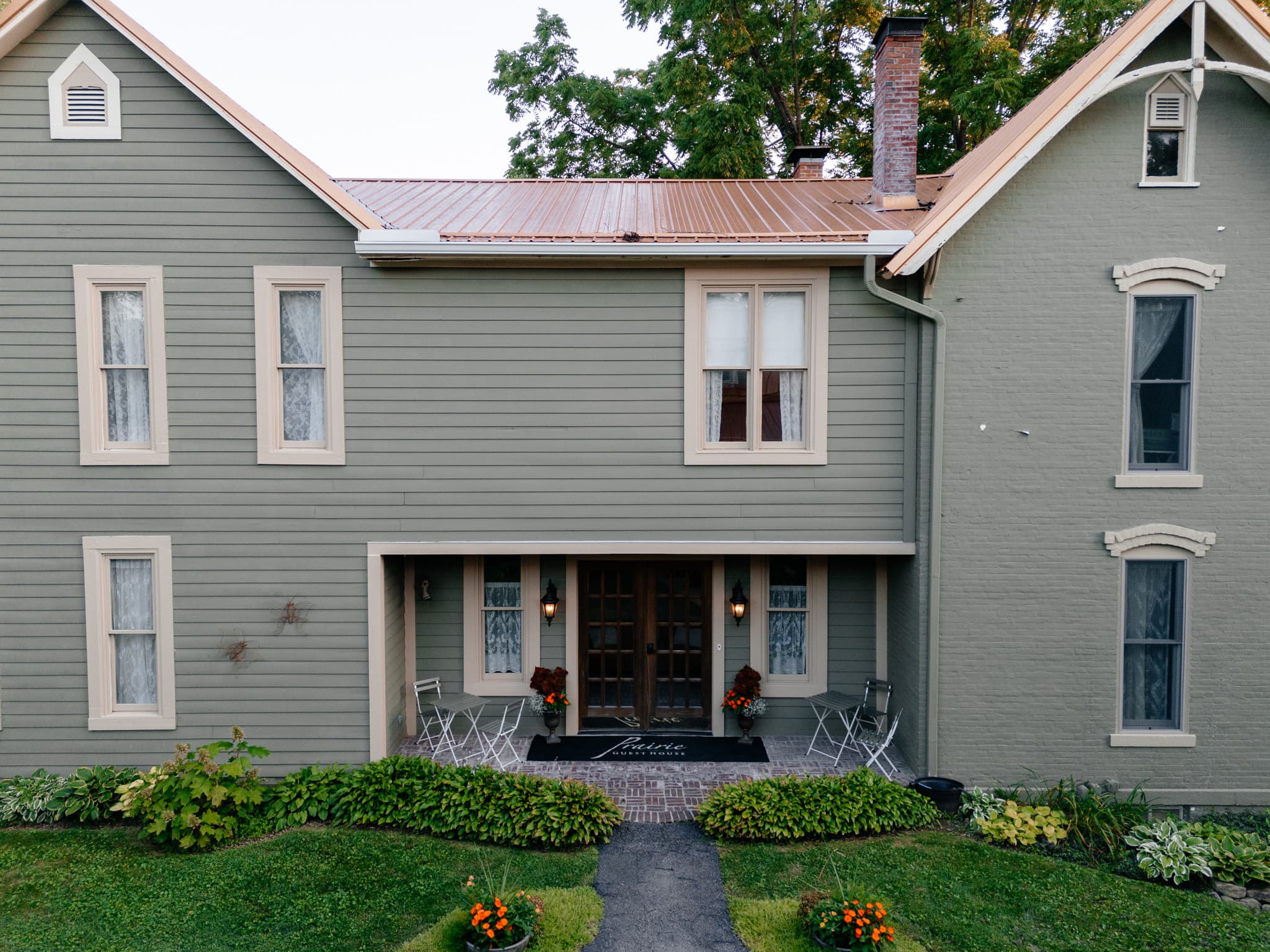 A charming, two-story gray house featuring a welcoming front porch with seating and floral decorations.