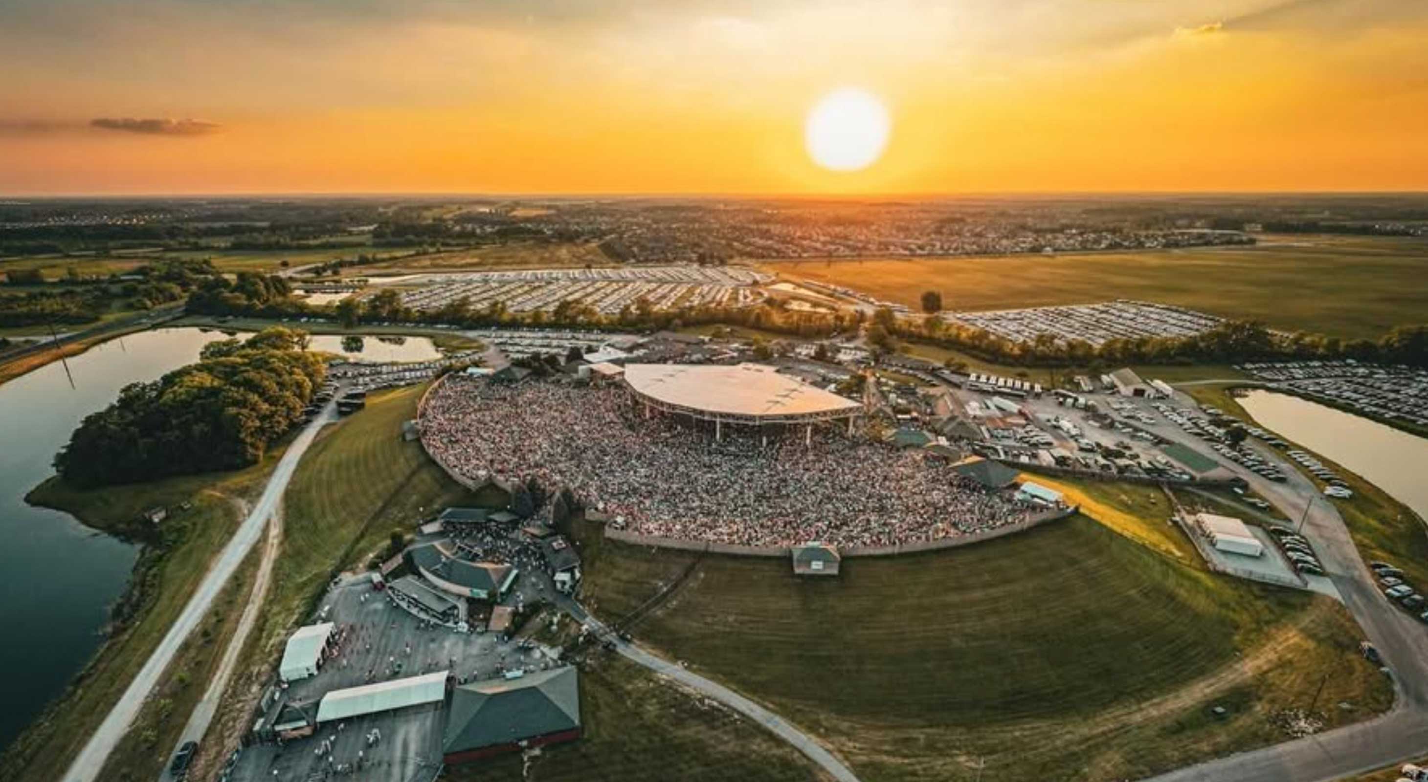 Aerial view of a large outdoor concert with an audience gathered beneath a sunset. Aerial view of a large outdoor concert with an audience gathered beneath a sunset.