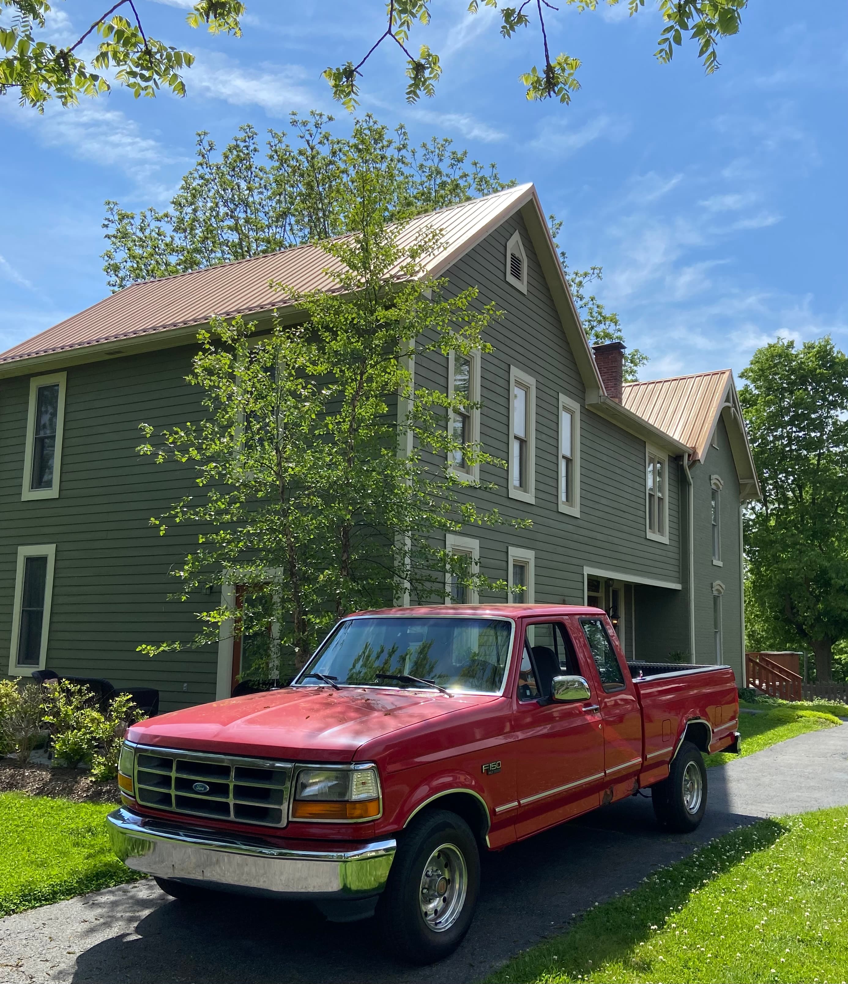 A red pickup truck parked beside a green house under a clear blue sky.