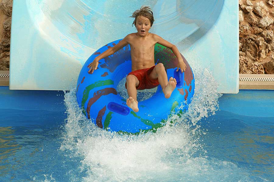A boy joyfully slides into the water on a colorful inflatable tube.