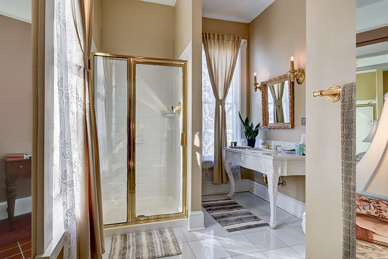 A well-lit bathroom featuring a glass shower, decorative mirror, and a white vanity with plants.