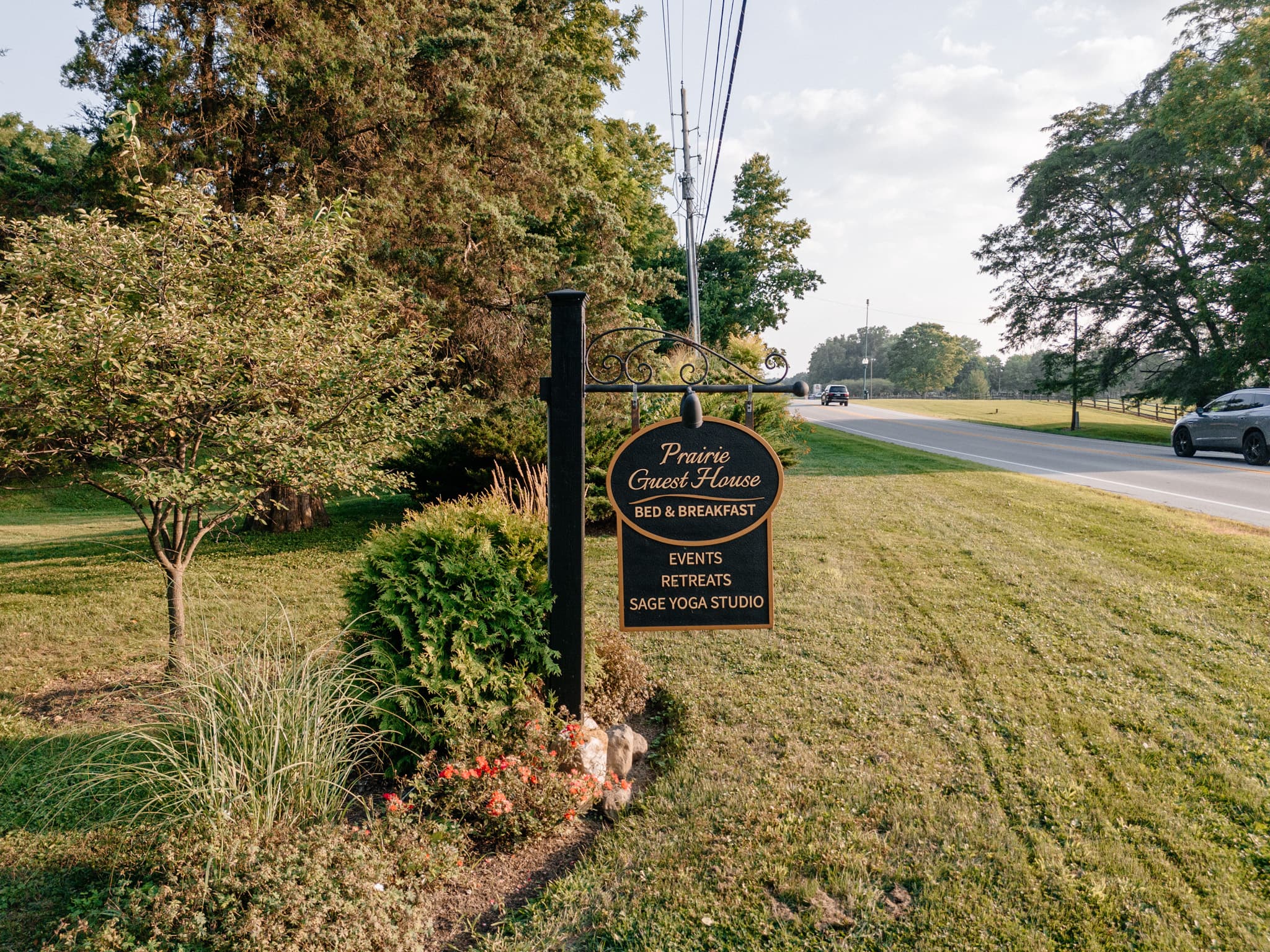 Sign for Prairie Guest House Bed & Breakfast, featuring offerings for events, retreats, and a yoga studio, set amidst greenery.