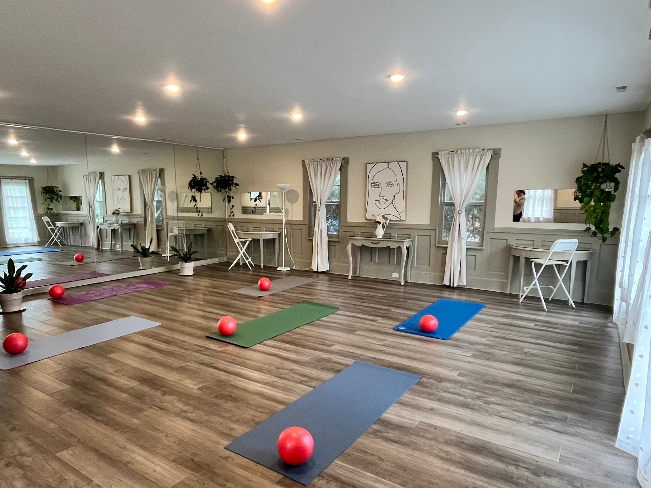 A bright, airy fitness studio featuring colorful mats, red exercise balls, and large mirrors.