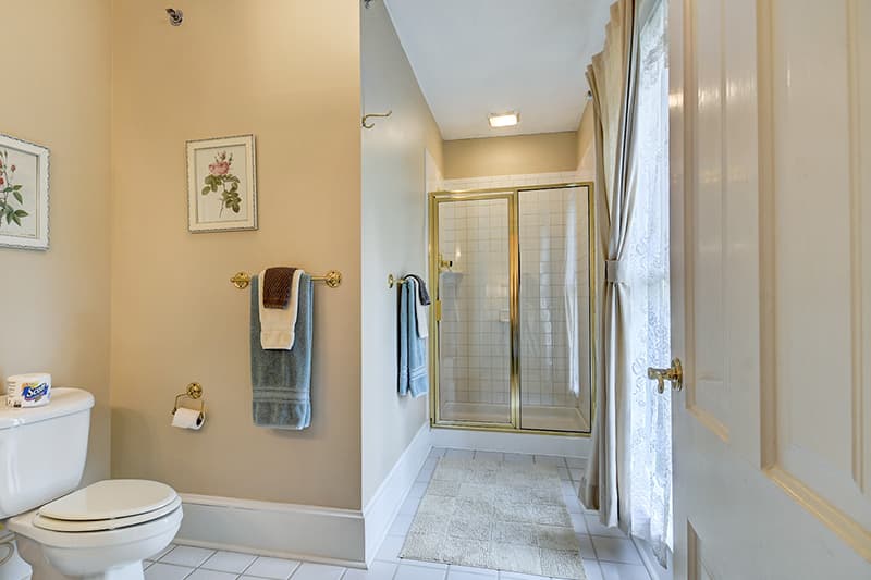 A well-lit bathroom featuring a toilet, shower with glass doors, towels, and decorative wall art.
