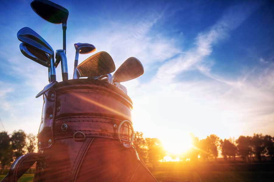 A leather golf bag filled with clubs against a sunset backdrop.