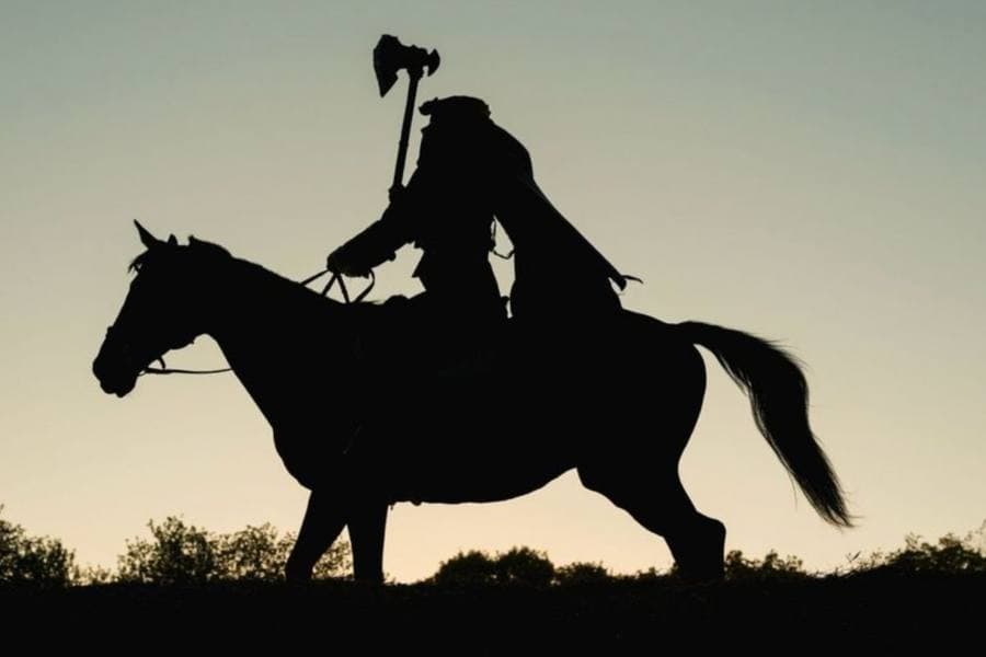 A silhouetted figure on horseback wields an axe against a twilight sky.