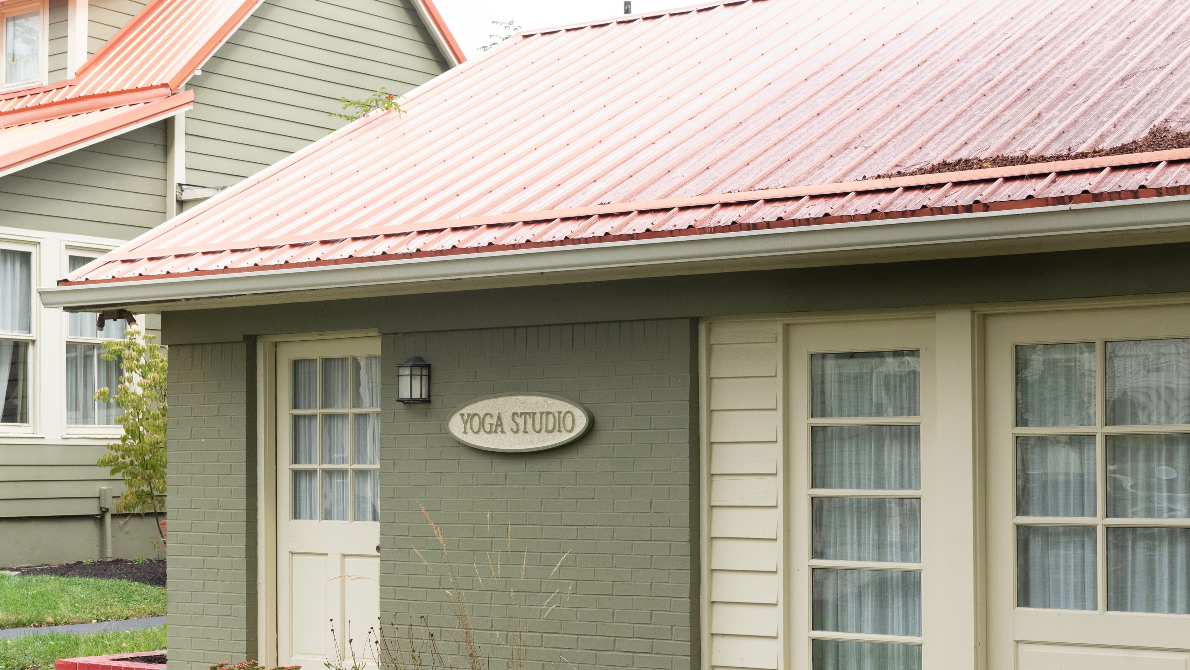 A cozy yoga studio with a sign, featuring a green exterior and red metal roof.
