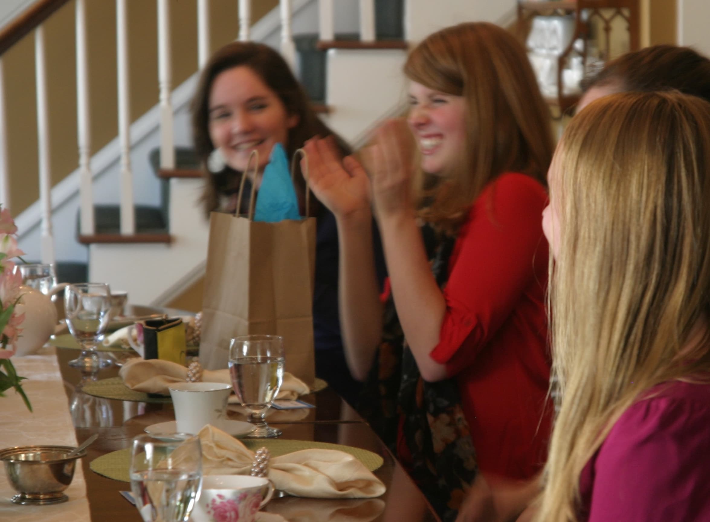 A group of women sitting at a table, smiling and clapping during a gathering.