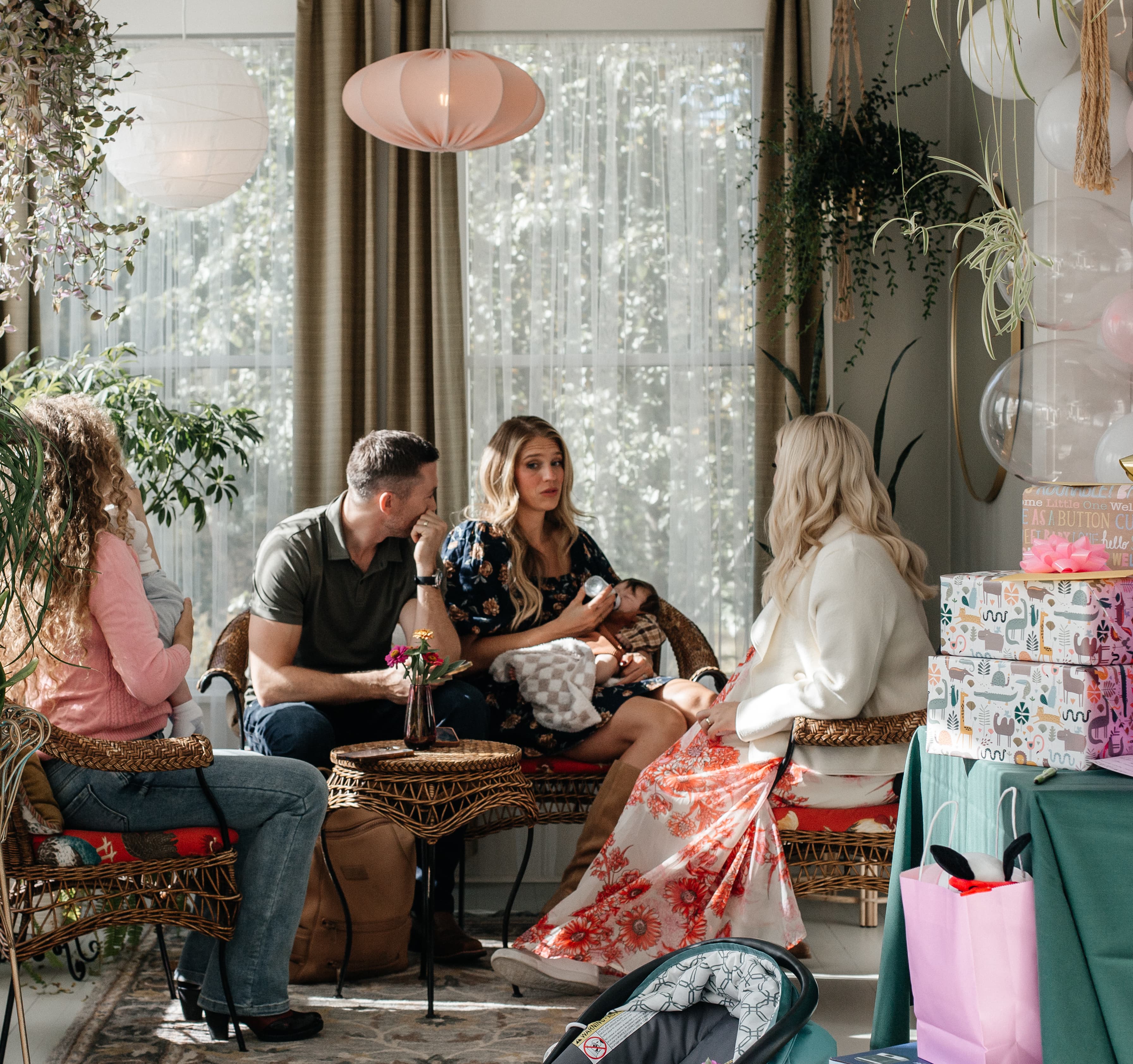 A group of four people sits in a brightly decorated room, engaged in conversation, with gifts and colorful decorations nearby.