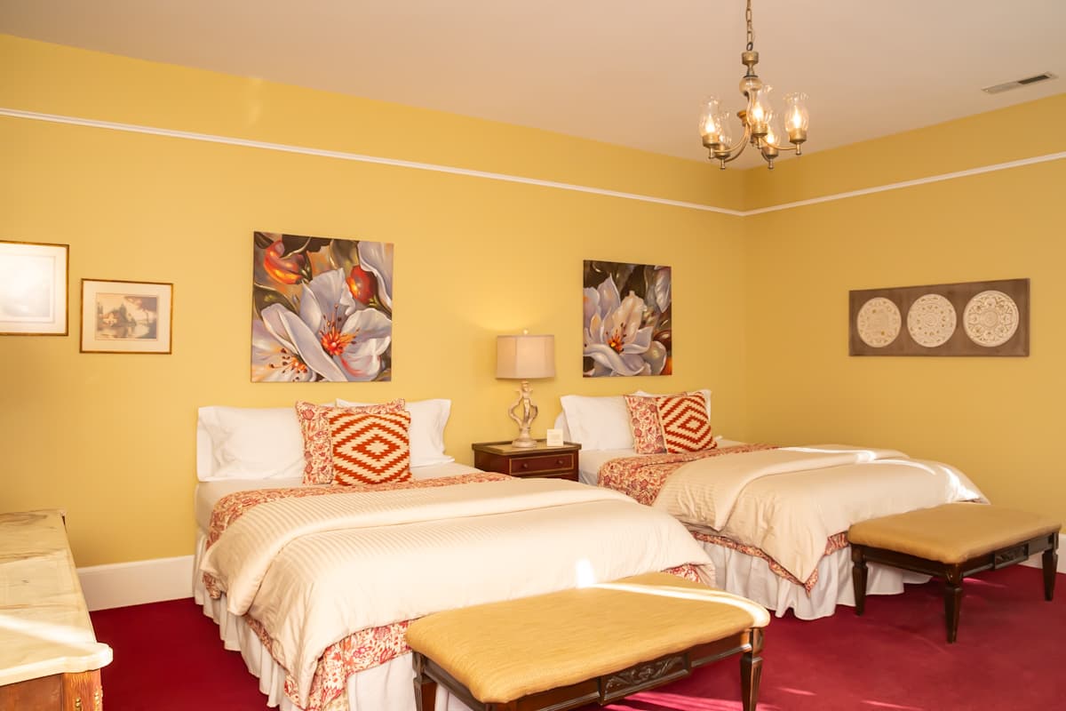 A cozy guest room featuring two beds, yellow walls, and floral artwork.