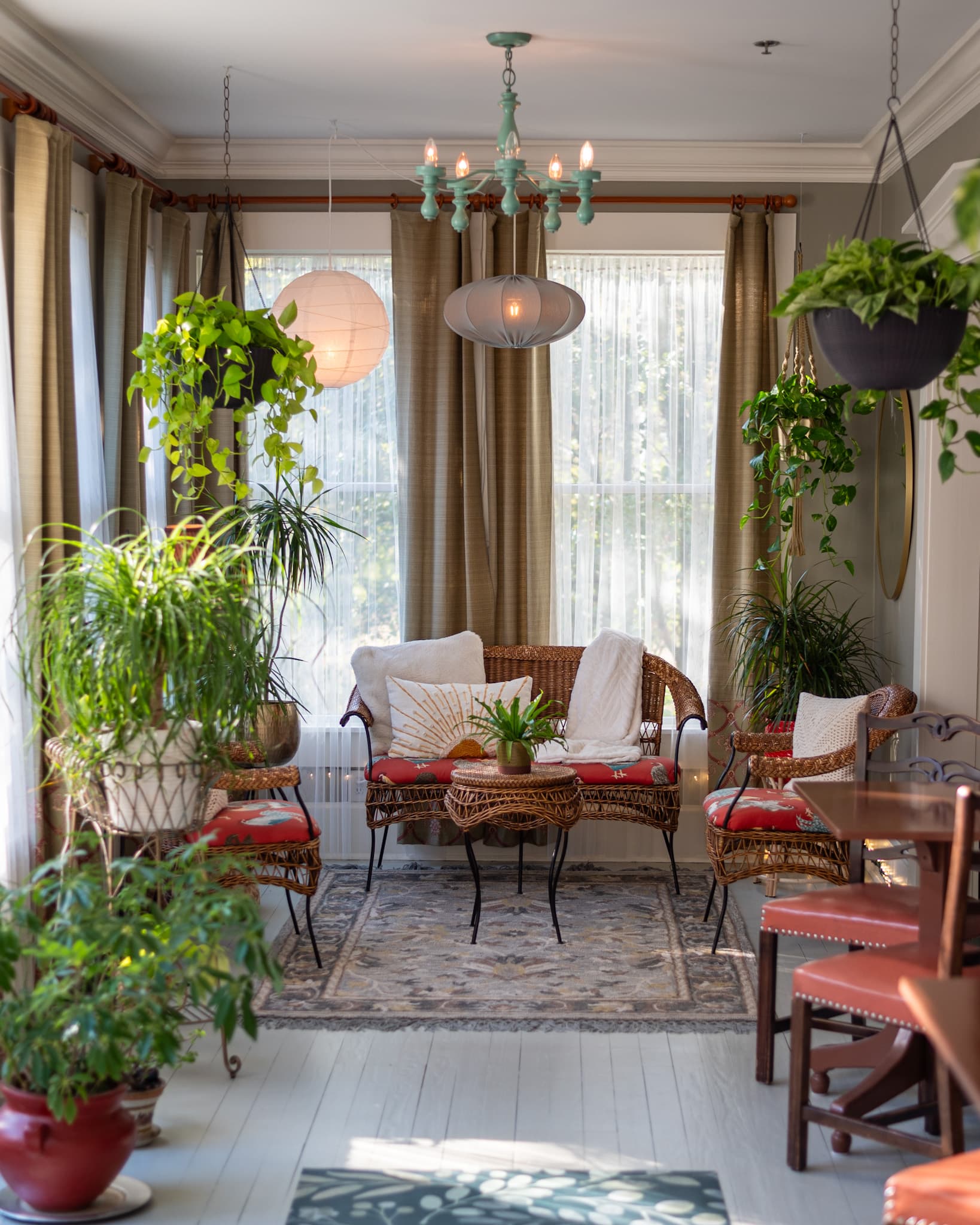 A cozy, brightly lit sunroom filled with plants and inviting wicker seating.
