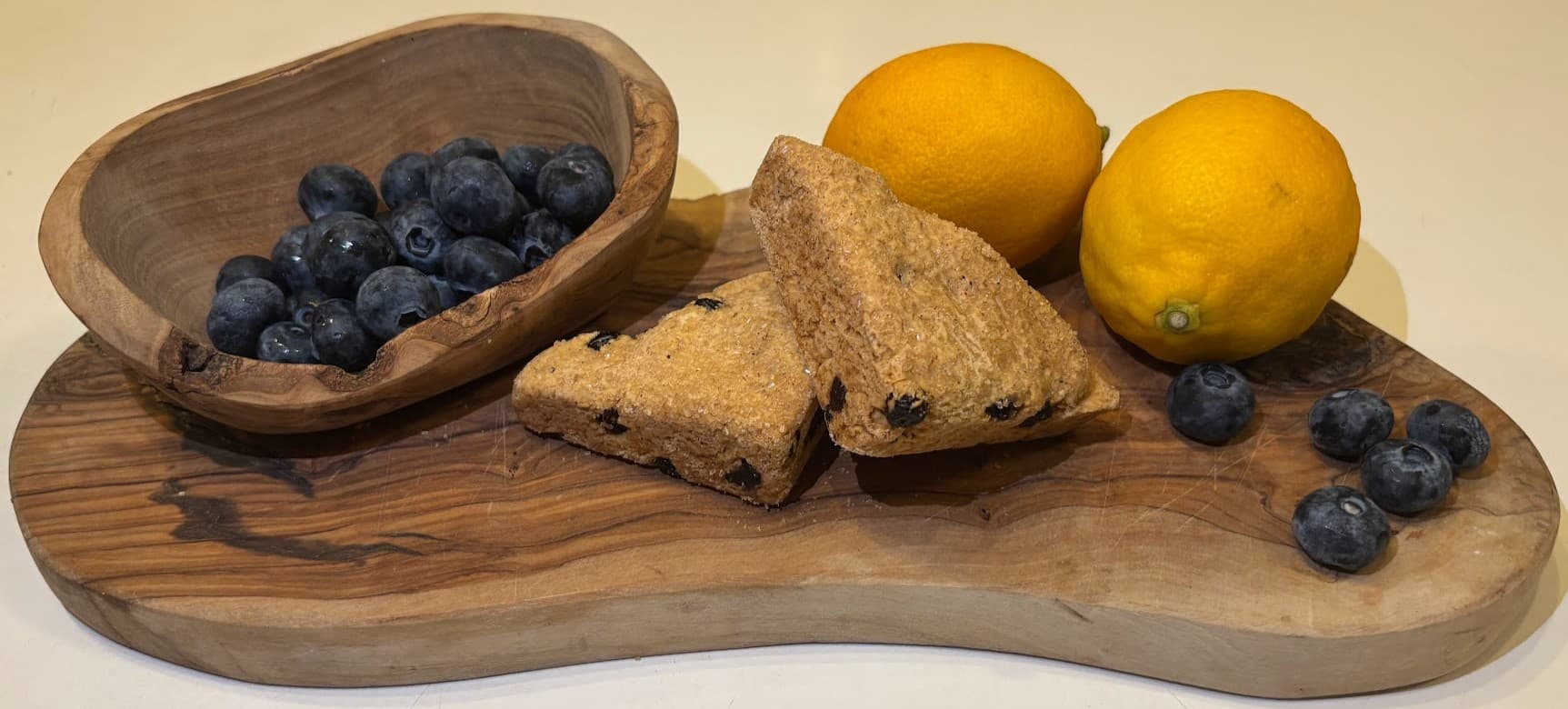 View of a platter holding blueberry lemon scones, fresh lemons, and fresh blueberries.