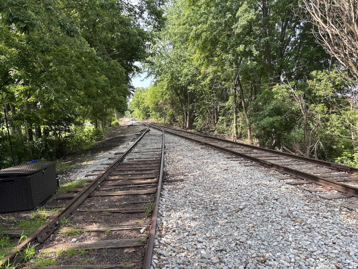View of two shaded railroad tracks merging into one railroad track.